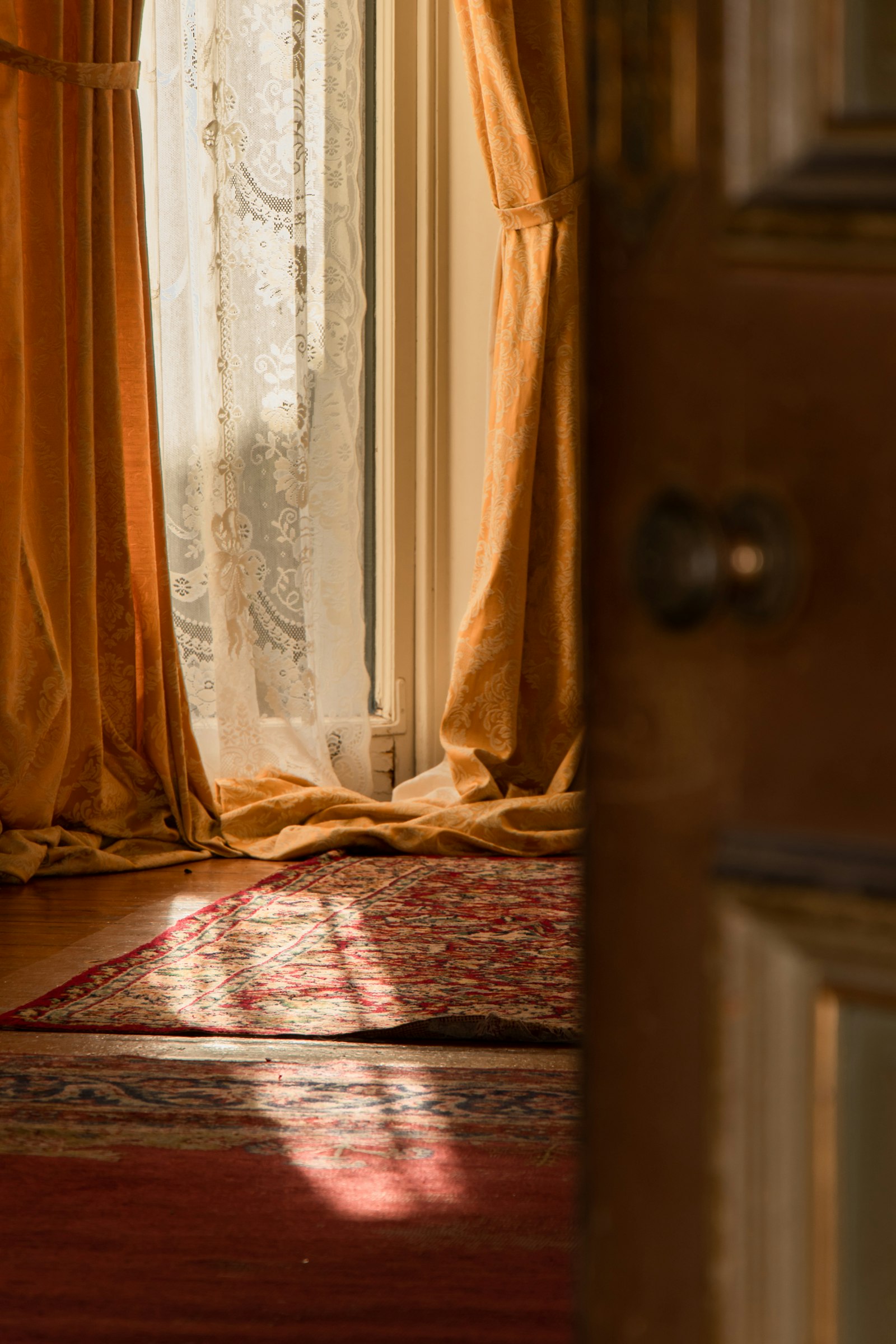 Warm brocade curtains framing a tall window with afternoon sunlight spilling across an antique carpet