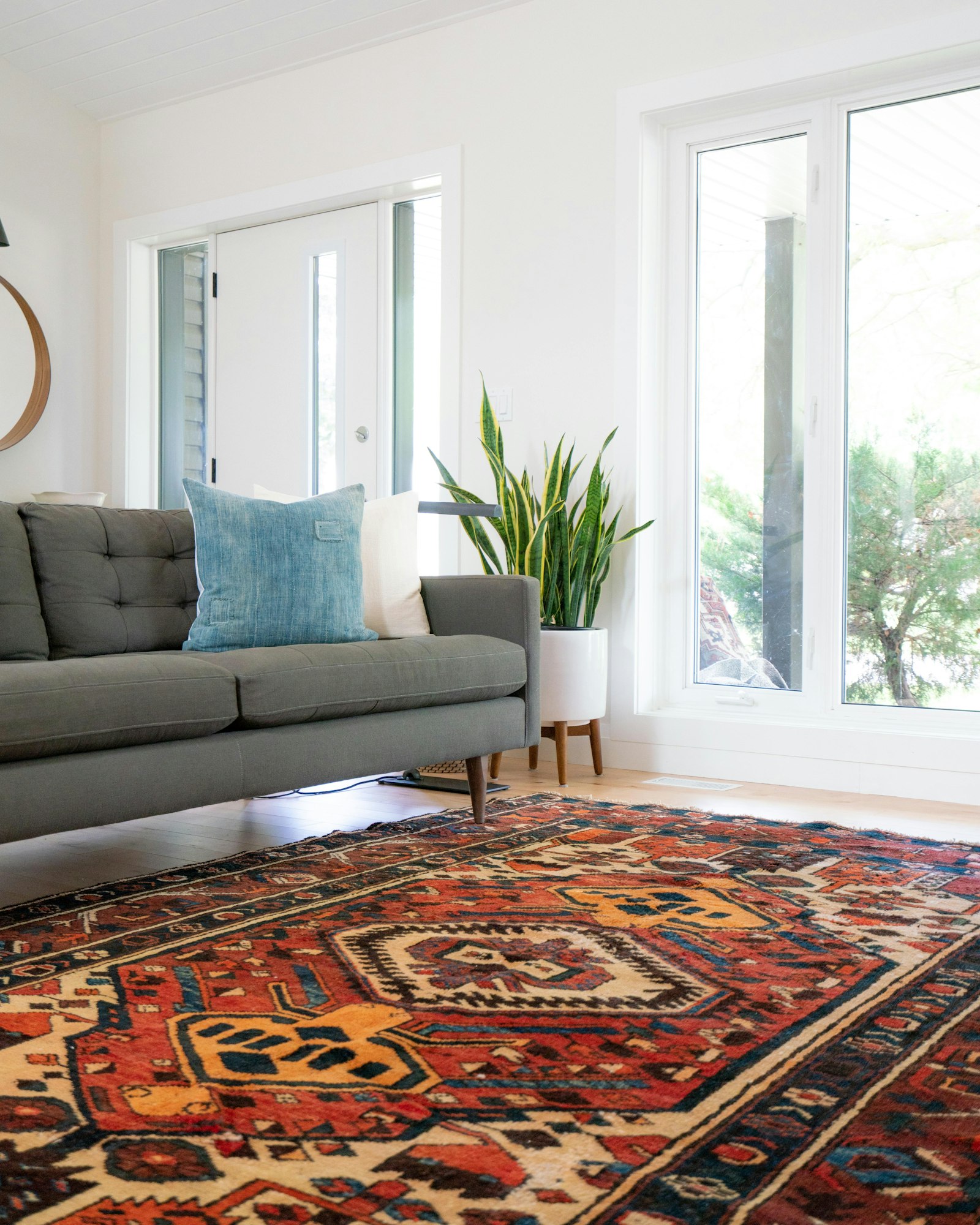 Rust and blue kilim rug on wood floor with a grey linen sofa and snake plant