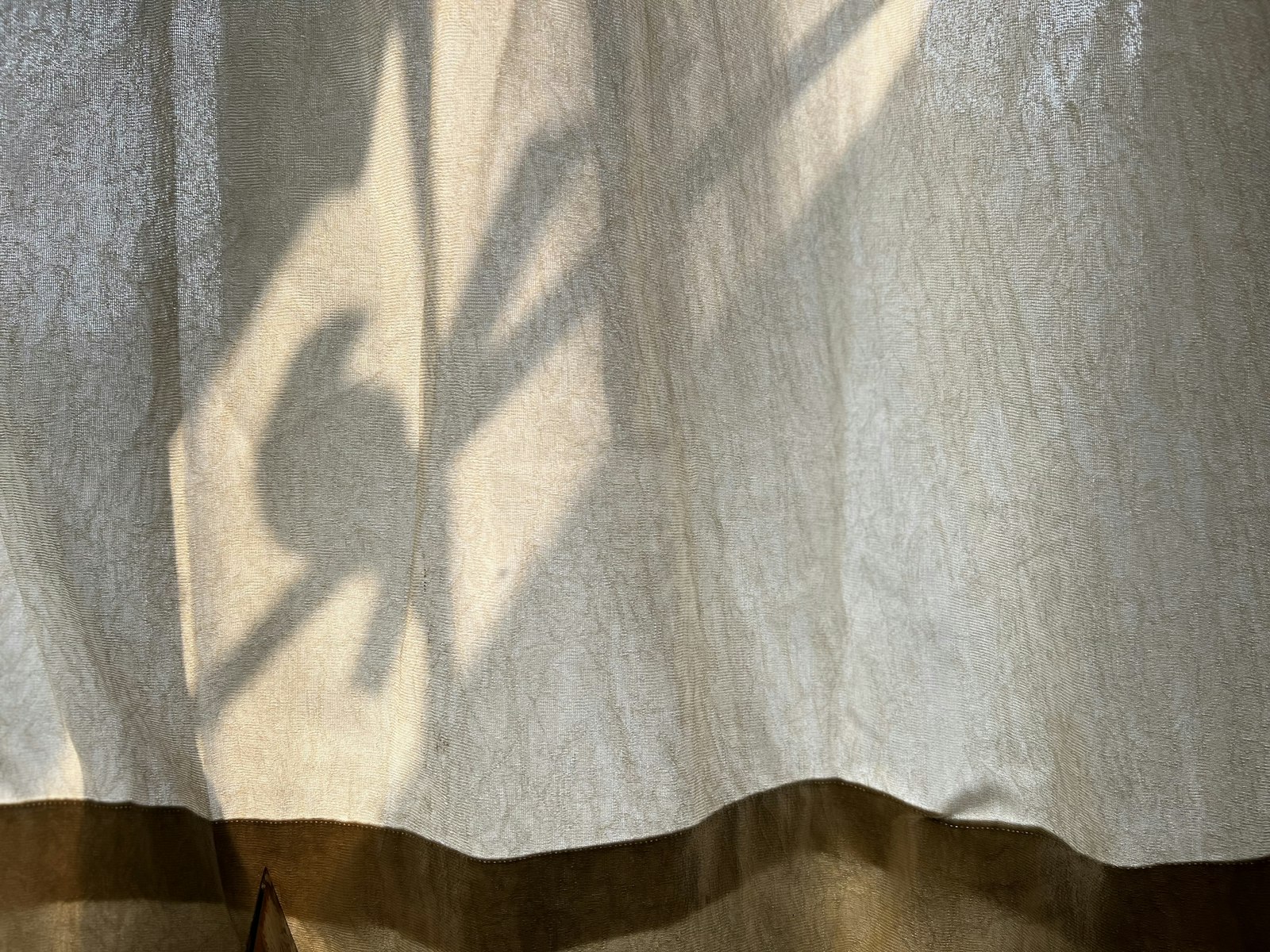 A warm tan sheer curtain catching soft plant shadow in afternoon light