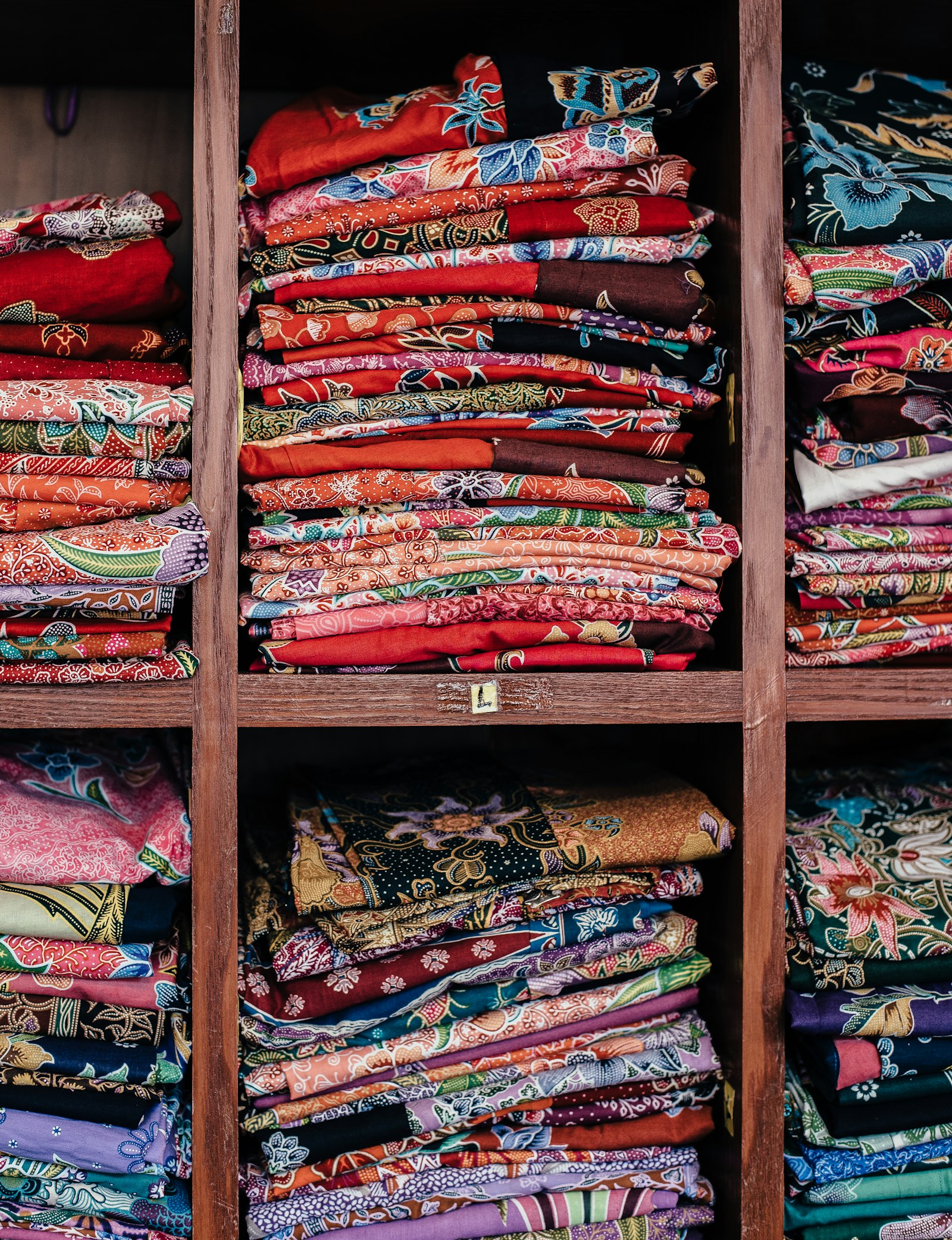 Warm-wood cubby shelves stacked with folded printed fabrics — the fabric wall