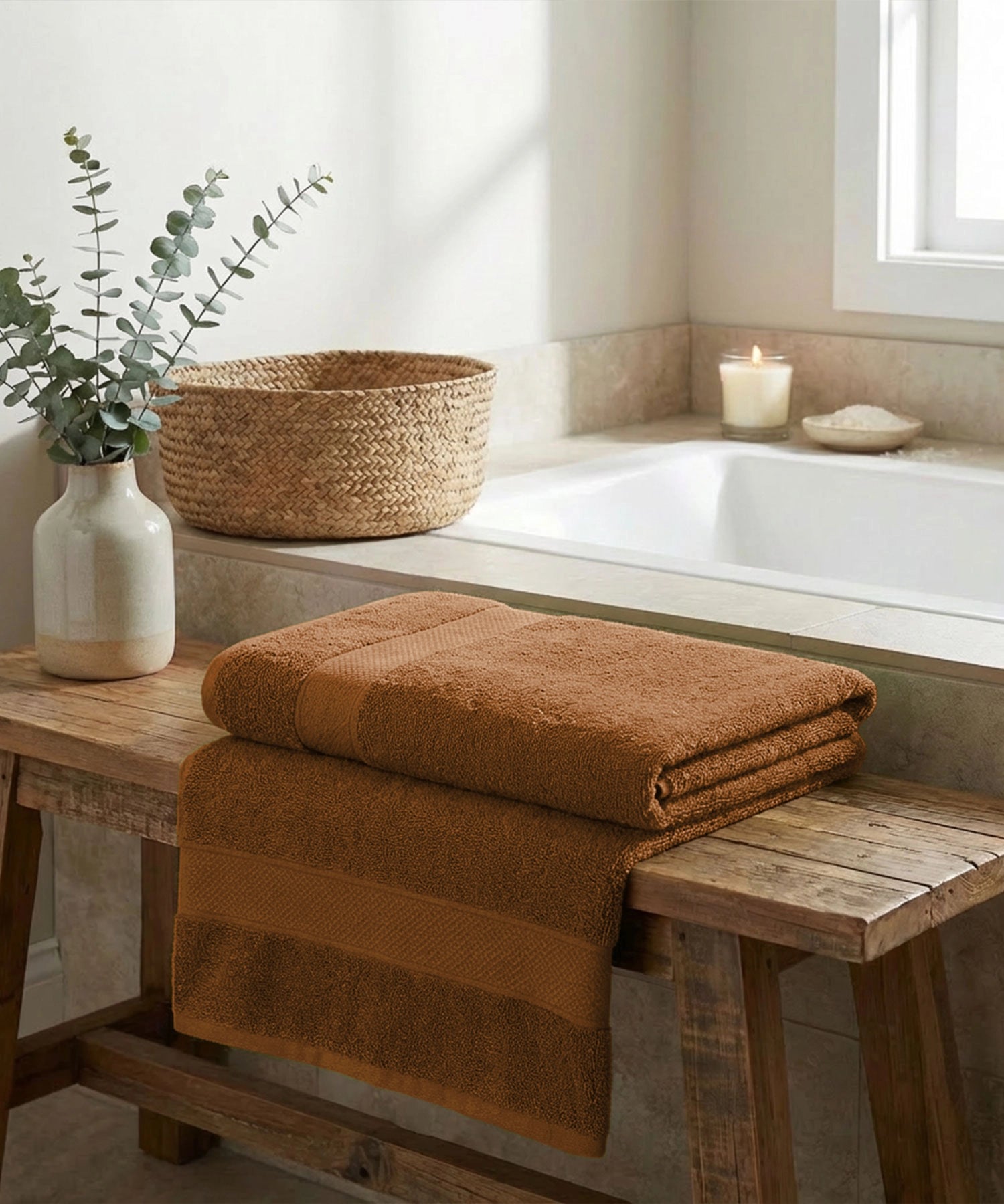 Folded cotton towels on a rustic wooden bench beside a tub, warm daylight